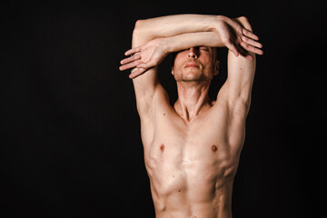 A man with a beautiful body poses in the studio against a black background.