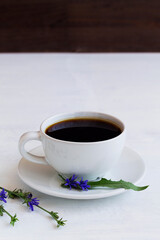 chicory drink in white cup decorated blue chicory flowers on white wooden background. healthy. coffee substitute. hot drinks. copy space. vertical