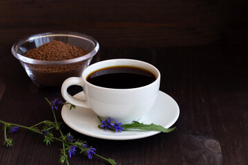 hot chicory drink in white cup with blue chicory flowers and Ground chicory root on dark brown wooden background. healthy. coffee substitute. copy space.