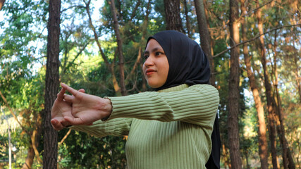 Muslim Women stretching arms and breathing fresh air in middle of pinewood forest while exercising
