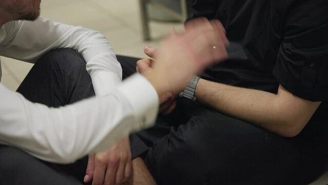 Close-up of a guy waiter in a white shirt supports a professional cook and pats him as a sign of support while sitting on the floor in the kitchen in a restaurant