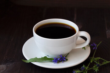 chicory drink in white cup with blue chicory flowers on dark brown wooden background. healthy. coffee substitute. copy space.
