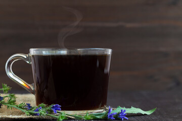 glass cup of hot chicory drink with blue chicory flowers on dark brown wooden background. healthy. coffee substitute. copy space.