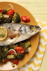 Delicious baked fish and vegetables on yellow wooden table, top view