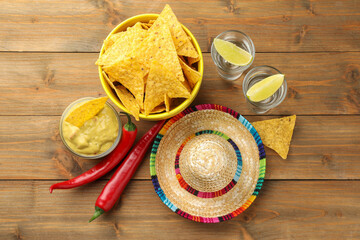 Mexican sombrero hat, tequila, chili peppers, nachos chips and guacamole on wooden table, flat lay