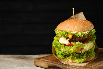 Burger with delicious patty on wooden table against dark background, space for text