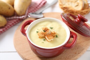 Tasty potato soup with croutons and rosemary in ceramic pot on white table, closeup
