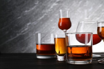 Different delicious liqueurs in glasses on dark wooden table, space for text