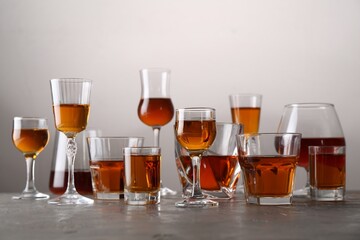 Different delicious liqueurs in glasses on grey table
