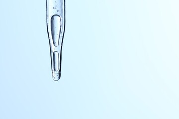 Dripping liquid from pipette on light blue background, closeup. Space for text