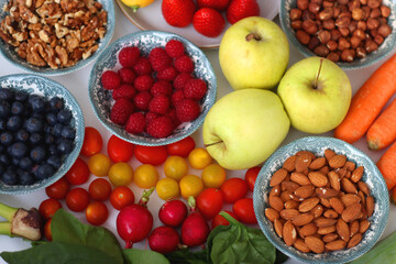 Apples, lemons, bananas, berries, carrots, leek, tomatoes, radishes, spinach and various nuts on white background. Healthy seasonal fruit and vegetable. Selective focus.