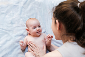 Top view of a baby lying on a blanket in a white diaper and his mother looking at him with love and affection. Little newborn girl laughs and experiences positive emotions. Mothers Day.