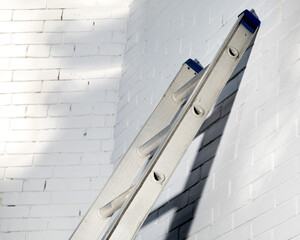 an aluminum extension ladder leaning against a white brick wall © SockaGPhoto