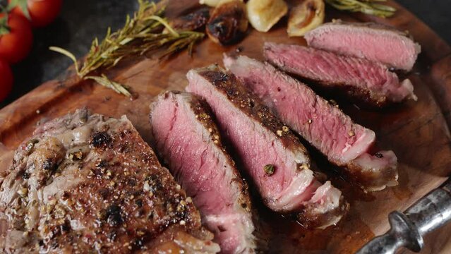 Pieces of hot ribeye steak served on the wooden board. Medium steak slices.