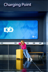 Young woman waiting near charging point station in airport terminal, charging mobile device. Woman...
