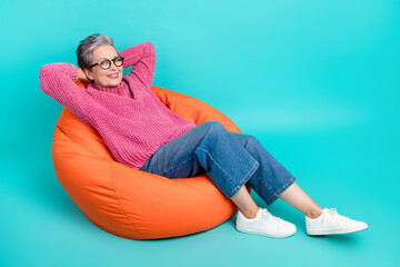 Full size photo of satisfied person dressed knitwear jumper jeans lay on pouf arms behind head isolated on turquoise color background