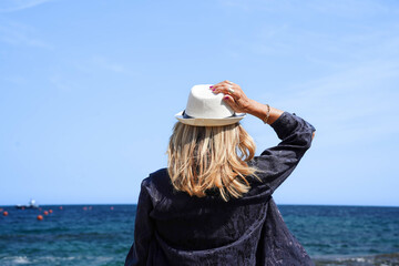 rear view of a mature woman wearing a hat and a black jacket looking at the horizon in summertime