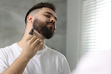 Handsome young man shaving with razor indoors. Space for text