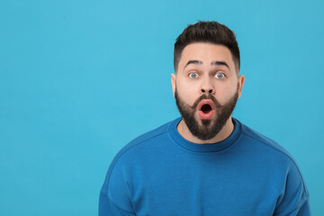 Surprised young man with mustache on light blue background. Space for text