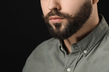 Handsome young man with mustache on black background, closeup