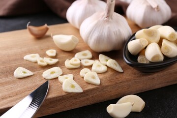 Aromatic cut garlic, cloves and bulbs on dark table, closeup