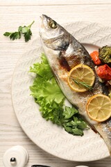 Delicious baked fish and vegetables served on wooden table, flat lay