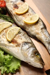 Delicious baked fish, lettuce and lemon on table, closeup