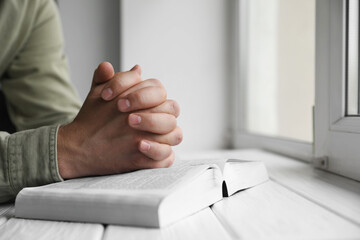 Religion. Christian man praying over Bible at white wooden the table, closeup