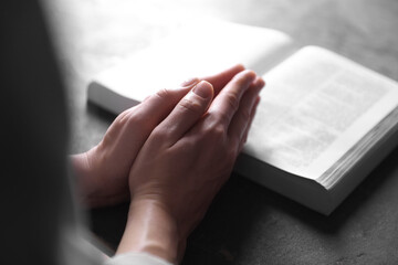 Religion. Christian woman praying over Bible at gray table, closeup