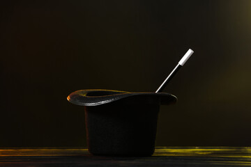 Magician's hat and wand on wooden table against dark background