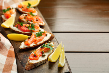 Tasty canapes with salmon, capers, lemon and cream cheese on wooden table, closeup. Space for text