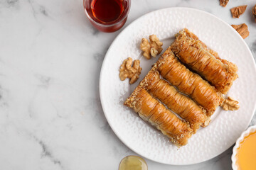 Eastern sweets. Pieces of tasty baklava, walnuts and tea on white marble table, flat lay. Space for...