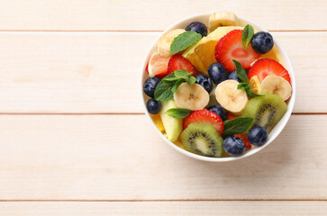 Tasty fruit salad in bowl on wooden table, top view. Space for text