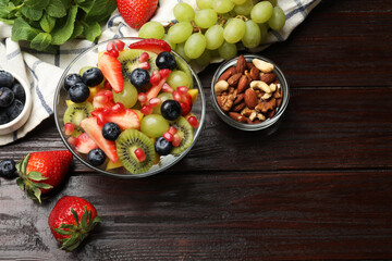 Tasty fruit salad in bowl and ingredients on wooden table, flat lay. Space for text