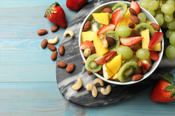 Tasty fruit salad in bowl and ingredients on light blue wooden table, flat lay. Space for text