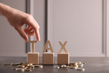 Woman with word Tax, wooden cubes and coins at grey table, closeup. Space for text