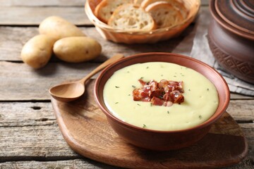 Tasty potato soup with bacon and rosemary in bowl served on wooden table