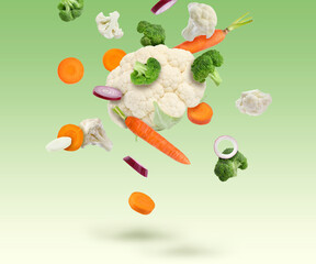 Different fresh vegetables in air on green gradient background
