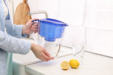 Woman with water filter jug in kitchen, closeup
