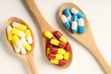 Antibiotic pills and spoons on white background, flat lay