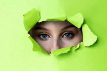Niebieskie oczy patrzące przez dziurę w zielonym kartonie