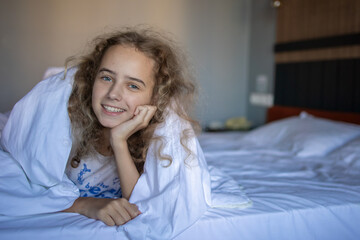 A blonde cute teenage girl in a white plaid on a large comfortable bed in an amazing cozy hotel...