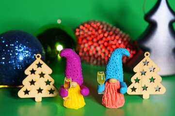 Two toy dwarfs made of plasticine with glasses of champagne on the background of Christmas decorations. New Year's holidays and Christmas. Decorations and decorations. Green background.