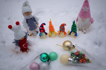 Fabulous toy characters in the winter forest. Four dwarfs with glasses of champagne and Christmas angels. Next to it are two glasses with Christmas balls.