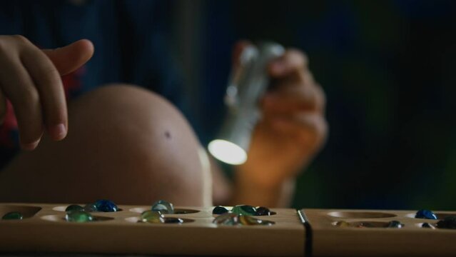 Person playing mancala by flashlight outdoors at night