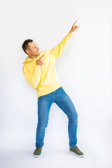 Cheerful Caucasian man in yellow hoodie dancing and pointing index fingers aside on yellow studio background