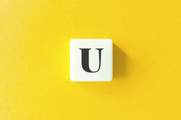 Capital Letter U. Text on Block Letter Tiles against Yellow Background.