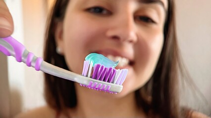 Close-up of a woman with a toothbrush applying toothpaste in the bathroom. Close-up of a girl's hands squeezing toothpaste on a purple brush. Smiling woman applying toothpaste to a clean toothbrush