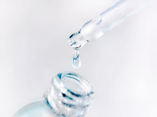 A drop falls from a pipette into a cosmetic bottle on a light background. Pipette with clear liquid. Facial skin care concept, beauty and health.