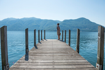 Woman standing and Waiting on a Pier on Lake Maggiore with Mountain in a Sunny Day in Brissago,...